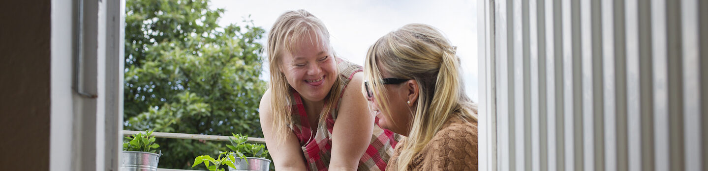 Mother and daughter with down syndrome picking cherry tomatoes on balcony